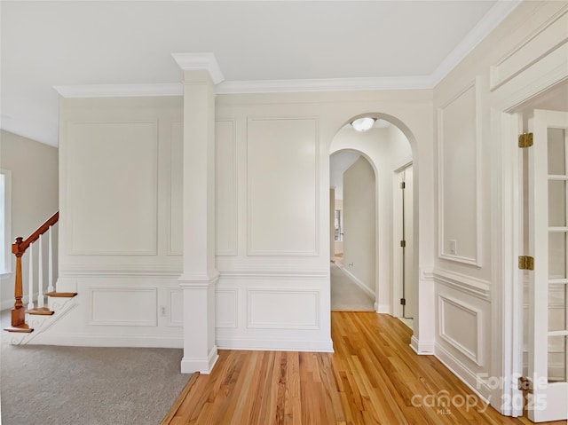 corridor featuring crown molding, light wood-type flooring, stairs, arched walkways, and a decorative wall