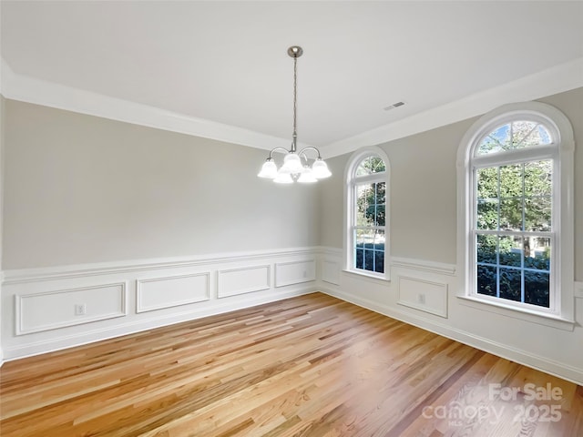 empty room with a wainscoted wall, visible vents, light wood finished floors, an inviting chandelier, and crown molding