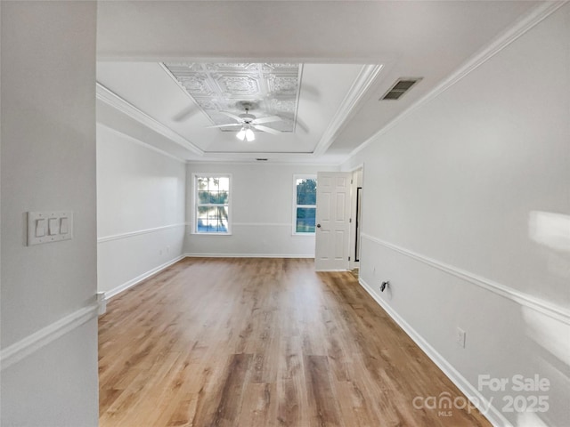 empty room with visible vents, a ceiling fan, baseboards, crown molding, and a raised ceiling