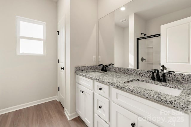 bathroom featuring a shower with shower door, wood finished floors, baseboards, and a sink