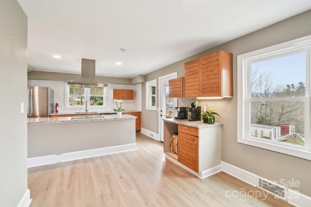 kitchen with island exhaust hood, visible vents, light wood finished floors, and freestanding refrigerator