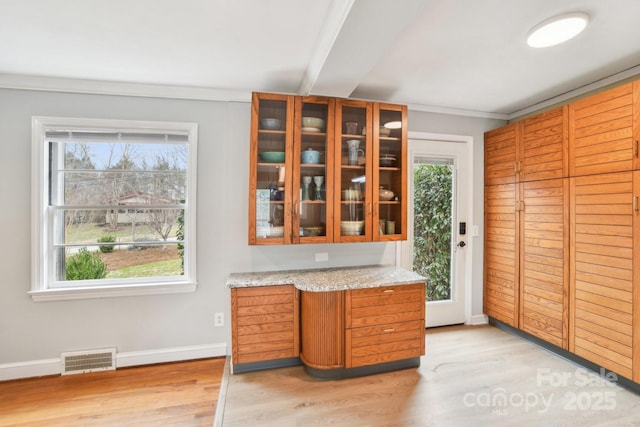 kitchen with visible vents, glass insert cabinets, baseboards, light wood-style flooring, and brown cabinets