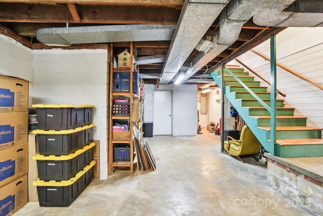 unfinished basement featuring stairs and concrete block wall