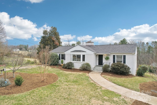 ranch-style home with a chimney, a front yard, and roof with shingles