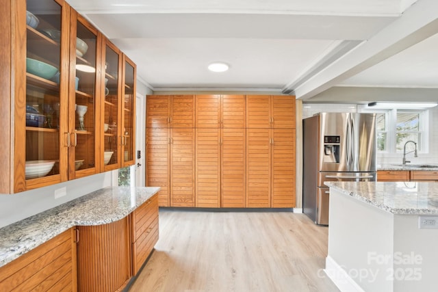 kitchen featuring glass insert cabinets, light stone countertops, light wood-style floors, stainless steel fridge, and a sink