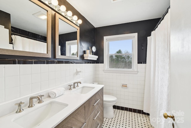 bathroom featuring double vanity, toilet, tile walls, and a sink