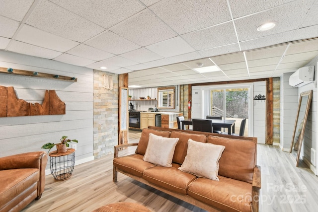 living area with a paneled ceiling, light wood-style floors, wooden walls, and a wall unit AC