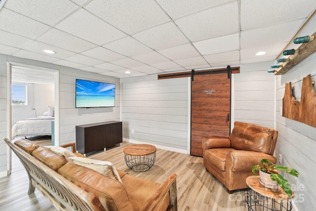 living room featuring wooden walls, a drop ceiling, a barn door, and wood finished floors