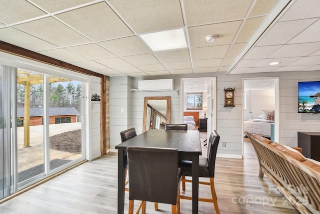 dining area featuring a drop ceiling, an AC wall unit, and light wood-style floors