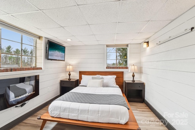 bedroom with wooden walls, wood finished floors, baseboards, and a paneled ceiling