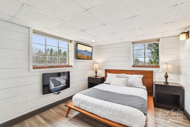 bedroom with a paneled ceiling, wooden walls, and wood finished floors