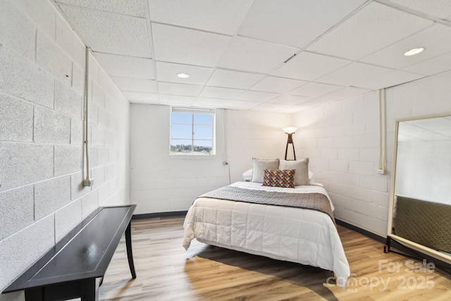 bedroom featuring recessed lighting, concrete block wall, a paneled ceiling, and wood finished floors