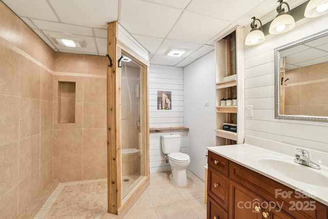 bathroom featuring toilet, a stall shower, tile patterned flooring, a paneled ceiling, and vanity