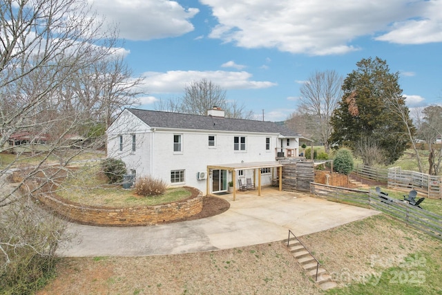 rear view of property with stucco siding, fence, concrete driveway, a chimney, and a patio area