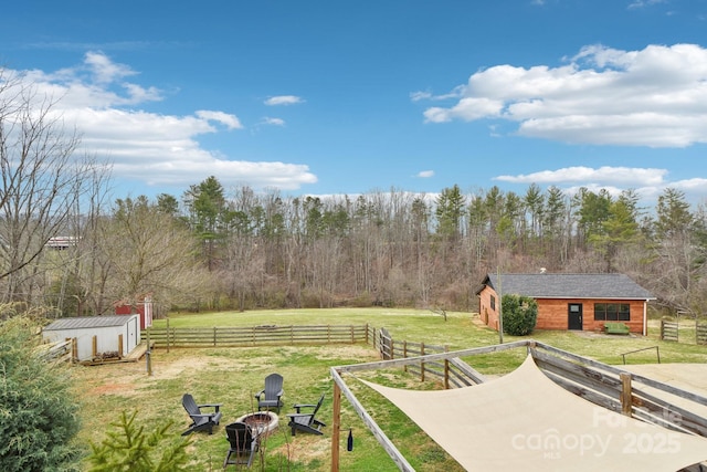 view of yard with a rural view, an outdoor structure, fence, and an outdoor fire pit