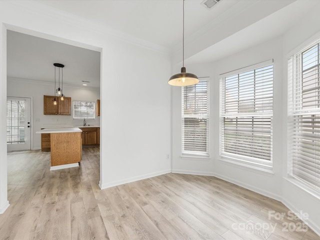 unfurnished dining area with light wood-style flooring, ornamental molding, a wealth of natural light, and a sink