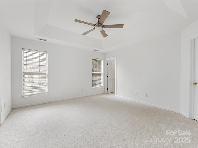 spare room featuring visible vents, baseboards, light colored carpet, a raised ceiling, and a ceiling fan