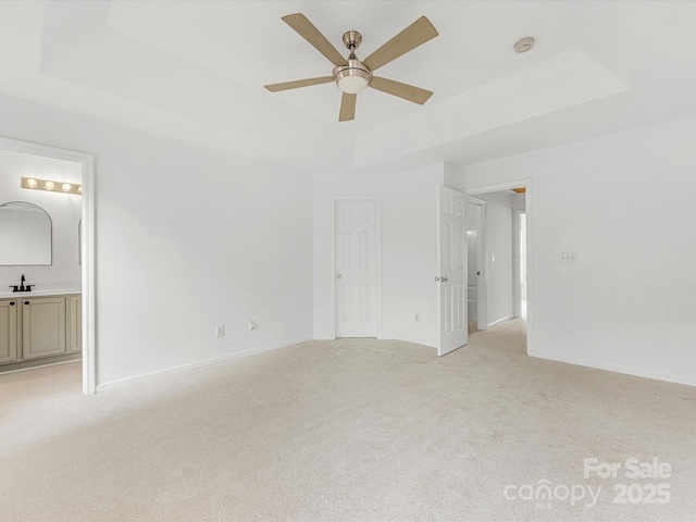 unfurnished bedroom featuring a raised ceiling, light carpet, baseboards, and a sink