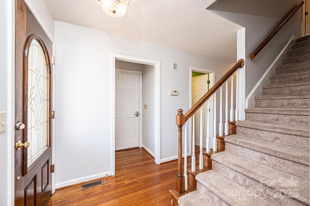 foyer with stairway, wood finished floors, visible vents, and a textured ceiling