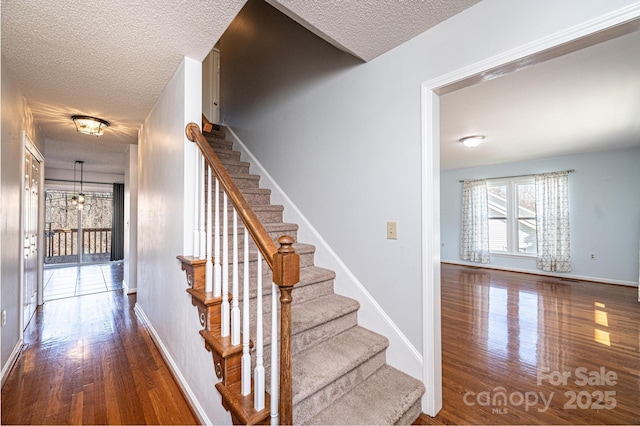 stairs featuring wood finished floors, baseboards, and a textured ceiling