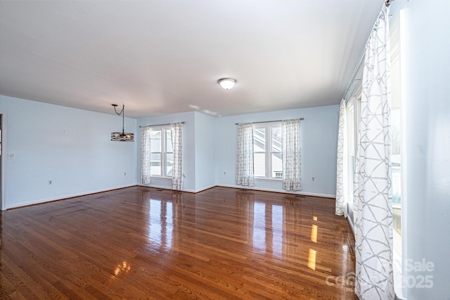 unfurnished room with an inviting chandelier, wood finished floors, and baseboards