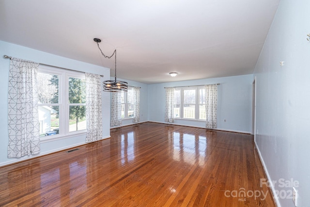 interior space with a notable chandelier, wood finished floors, visible vents, and baseboards