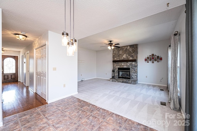 unfurnished living room featuring a ceiling fan, carpet floors, a fireplace, a textured ceiling, and tile patterned floors