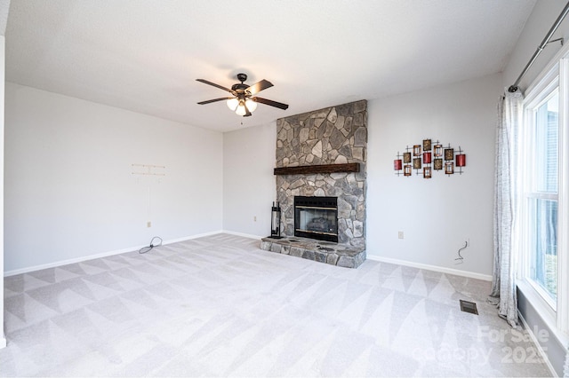 unfurnished living room with baseboards, visible vents, carpet floors, ceiling fan, and a stone fireplace