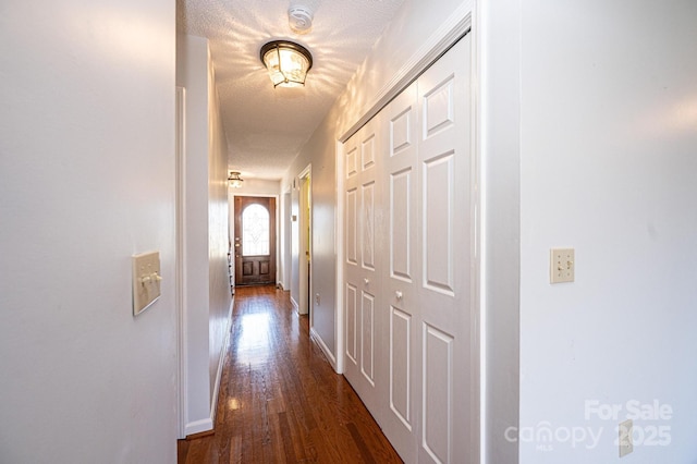 corridor with dark wood-type flooring, baseboards, and a textured ceiling