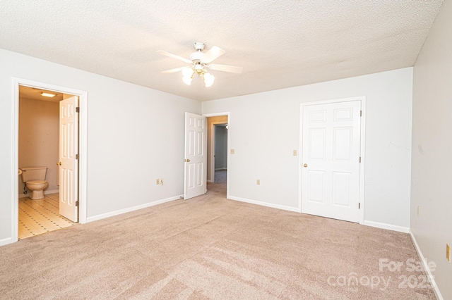 unfurnished bedroom with ensuite bath, light colored carpet, a textured ceiling, and baseboards