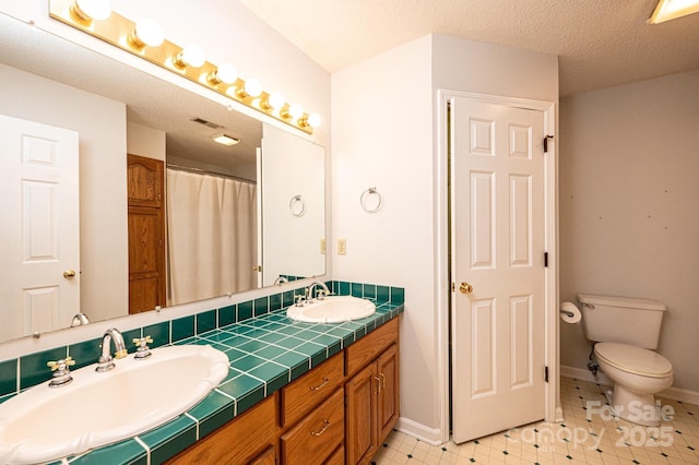 full bathroom featuring a sink, toilet, double vanity, and a textured ceiling