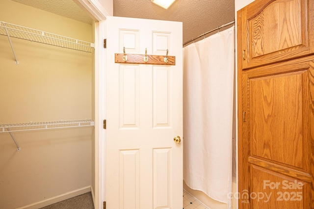 full bathroom with a spacious closet, a textured ceiling, and baseboards