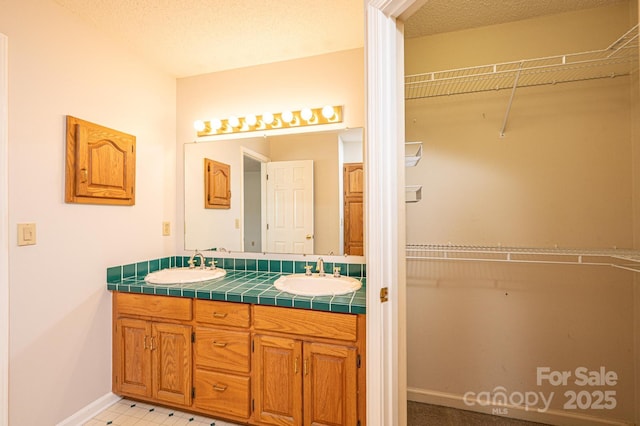 bathroom with a sink, a textured ceiling, a spacious closet, and double vanity