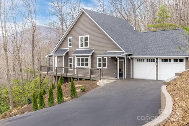 chalet / cabin with a wooden deck, driveway, roof with shingles, and an attached garage