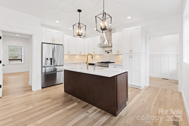 kitchen with wall chimney range hood, stainless steel fridge with ice dispenser, a chandelier, decorative backsplash, and white cabinets