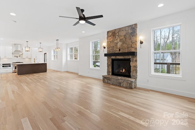 unfurnished living room with a ceiling fan, recessed lighting, light wood-style floors, a stone fireplace, and baseboards