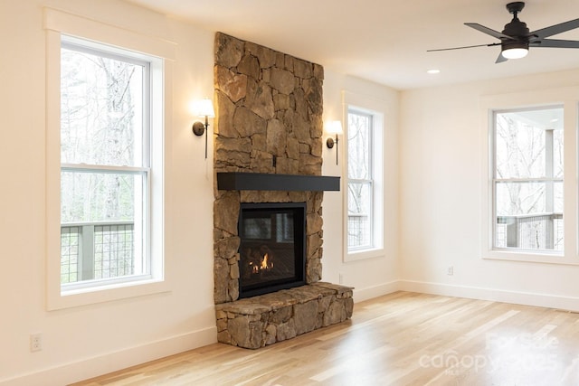 unfurnished living room with baseboards, a stone fireplace, wood finished floors, and a ceiling fan