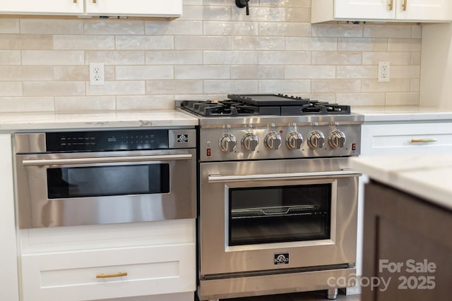 kitchen with tasteful backsplash, appliances with stainless steel finishes, white cabinetry, and light stone countertops