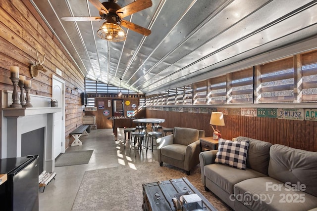 living area with wood walls, concrete flooring, ceiling fan, and vaulted ceiling