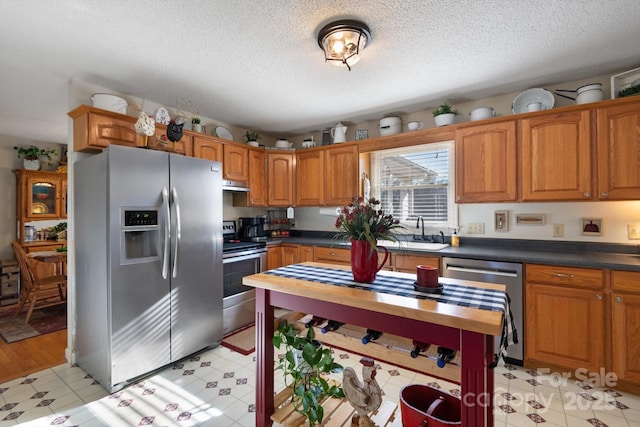 kitchen featuring brown cabinets, a sink, dark countertops, stainless steel appliances, and light floors