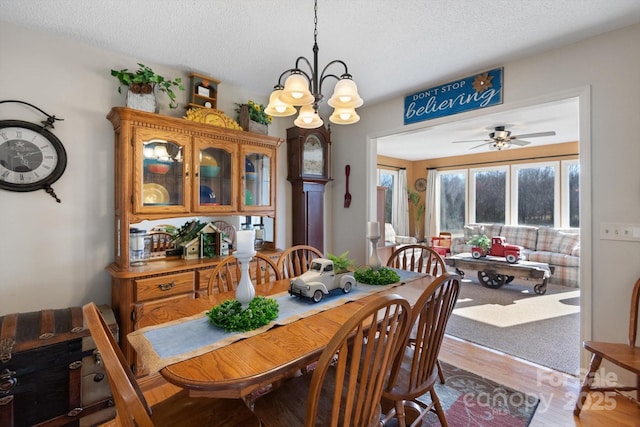 dining space with ceiling fan with notable chandelier, a textured ceiling, and wood finished floors