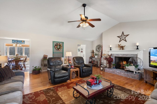 living area with ceiling fan with notable chandelier, a fireplace, lofted ceiling, and wood finished floors