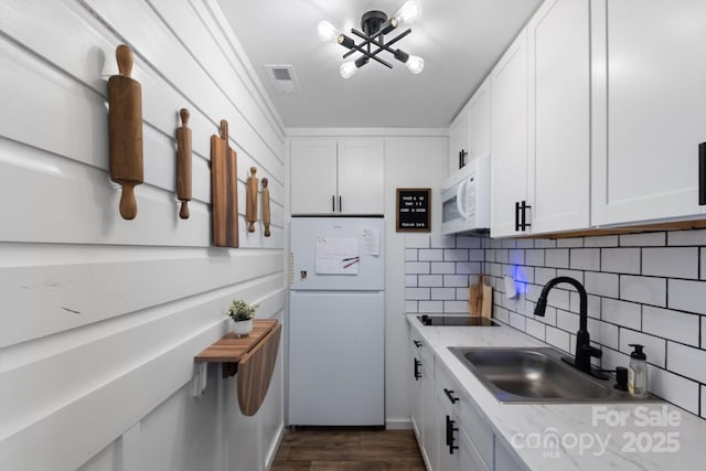 kitchen with visible vents, decorative backsplash, white cabinets, white appliances, and a sink