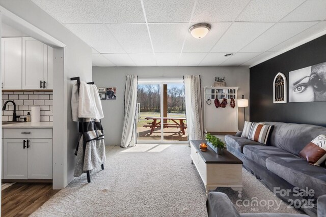 carpeted living area with a drop ceiling and a sink