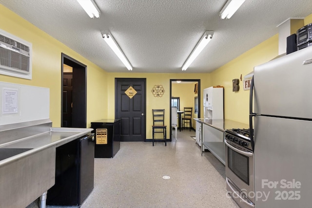 kitchen featuring a wall mounted air conditioner, light speckled floor, stainless steel appliances, and a textured ceiling