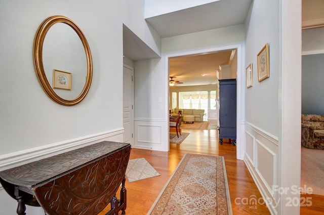 corridor with a decorative wall, wood finished floors, and wainscoting