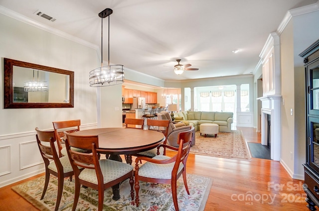 dining space with visible vents, a fireplace with flush hearth, ceiling fan, crown molding, and light wood-type flooring