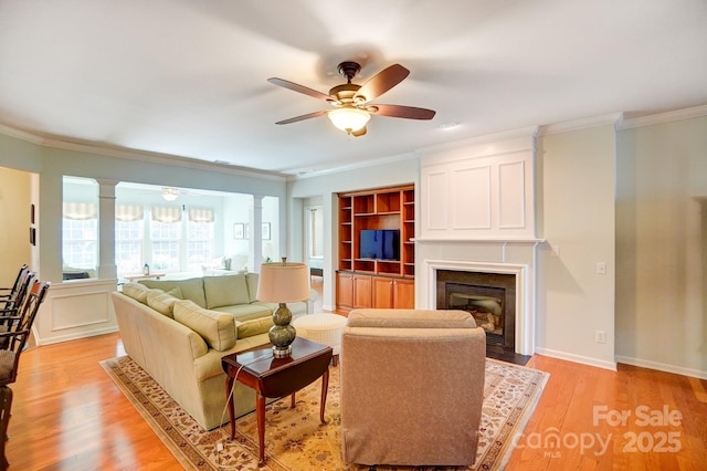 living room with crown molding, decorative columns, light wood-type flooring, and ceiling fan