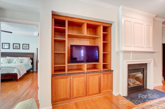 unfurnished living room featuring a glass covered fireplace, crown molding, and light wood-style floors