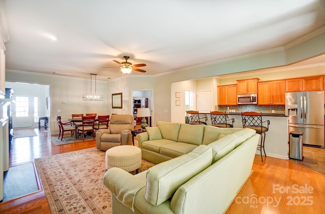 living room with ceiling fan with notable chandelier, light wood-type flooring, and ornamental molding